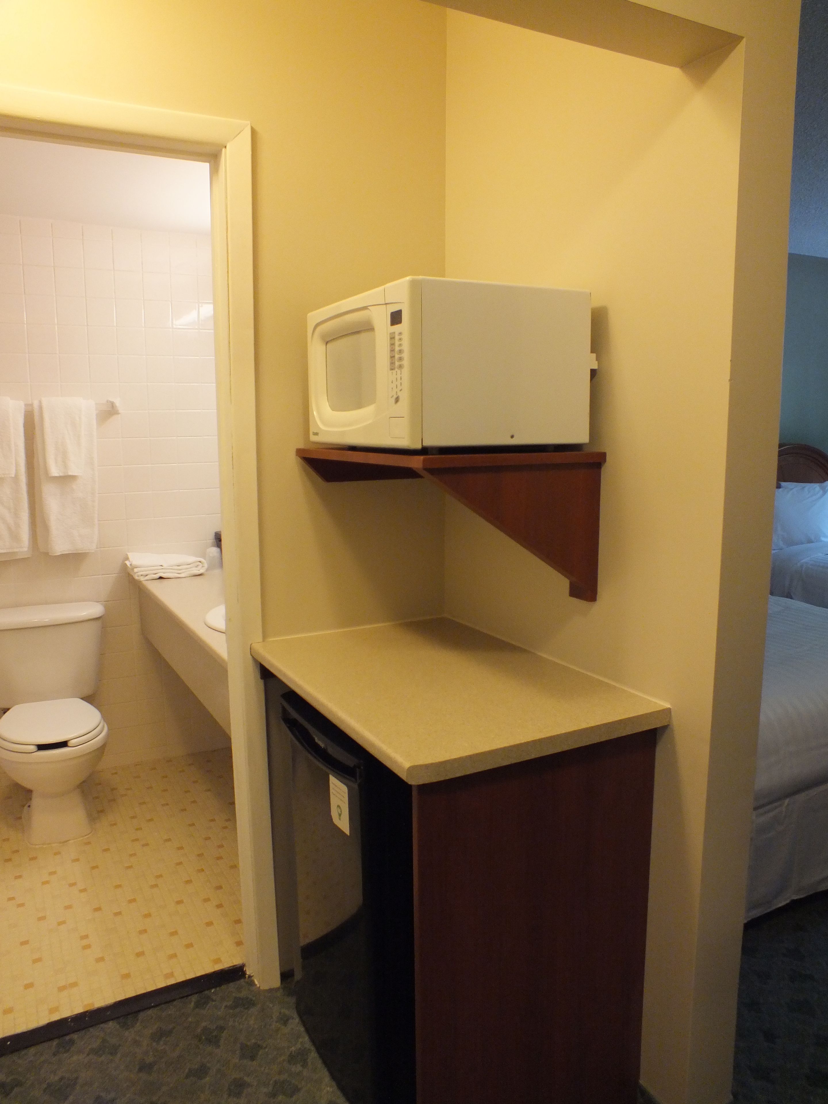 A compact bathroom with a toilet, sink, and a microwave on a shelf.