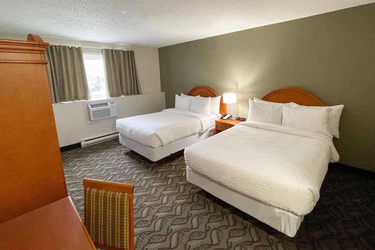 A hotel room with two beds, a window with curtains, an air conditioning unit, and a patterned carpet.