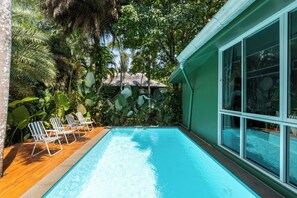 Una piscina con sillones de descanso, rodeada de exuberante vegetación tropical y una estructura con techo de paja.