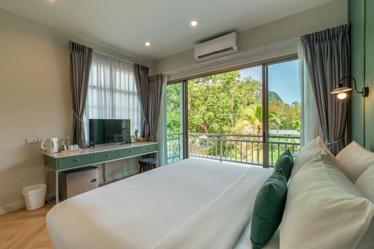 Habitación de hotel con una cama grande, un escritorio con televisor de pantalla plana, un mini refrigerador y un balcón con vista a zonas verdes.