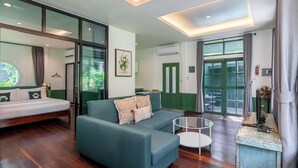 Une chambre d’hôtel moderne avec un lit, un canapé de couleur turquoise, une petite table ronde et une vue sur l’extérieur grâce à de grandes fenêtres.