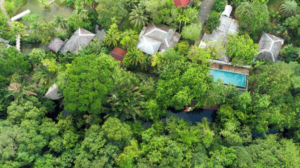 Vista aérea de una zona residencial con casas rodeadas de abundante vegetación, una piscina y un pequeño muelle con un bote.