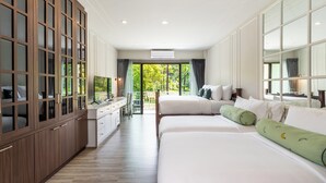 Une chambre d’hôtel dotée d’une grande armoire, d’un bureau avec une chaise, de deux lits avec des oreillers verts et offrant une vue sur la verdure par la fenêtre.