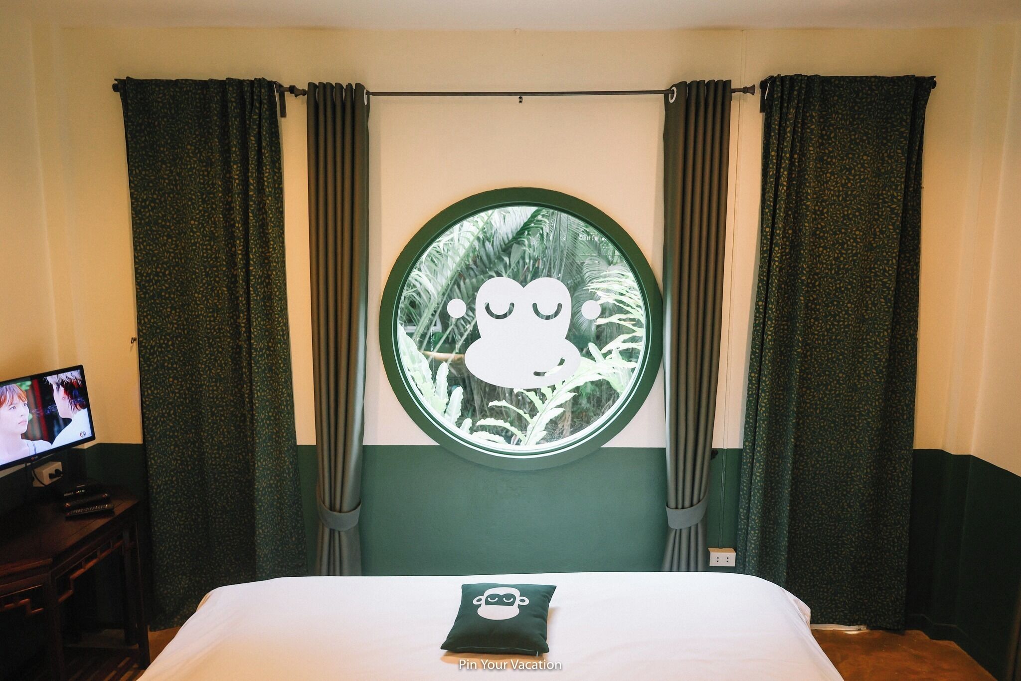 Una camera d'albergo con un letto, una finestra tonda con un personaggio dei cartoni animati, tende e una televisione su un mobile.