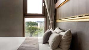 A hotel room with a bed, a view of a building and trees through a window, and a curtain.