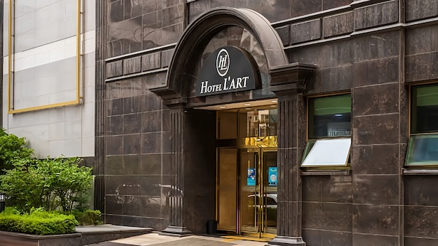 The entrance of Hotel L'Art with a dark facade, a gold-framed arch, and a glass door.