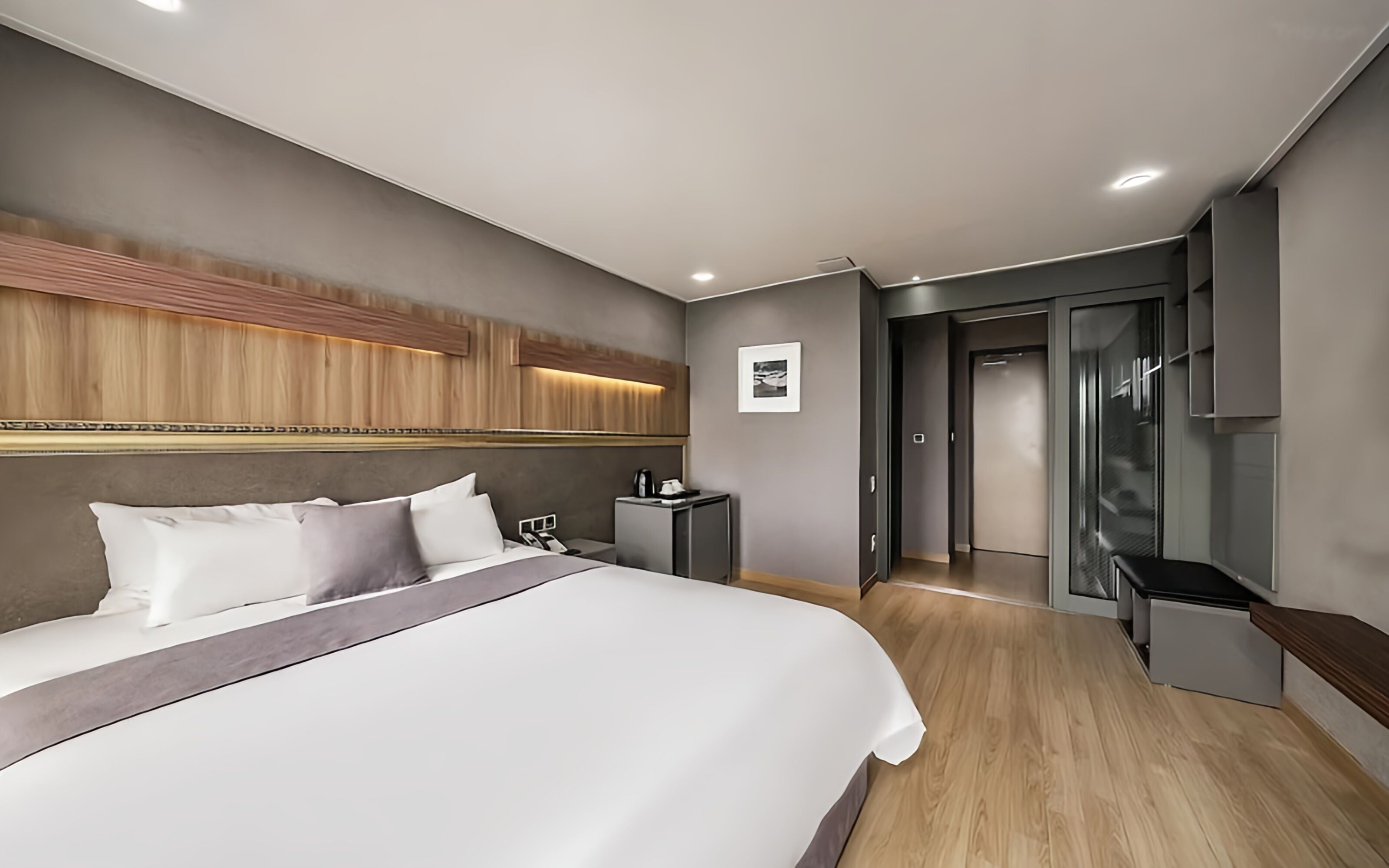 A modern hotel room with a large bed, a bedside table, a small cabinet, and a television.