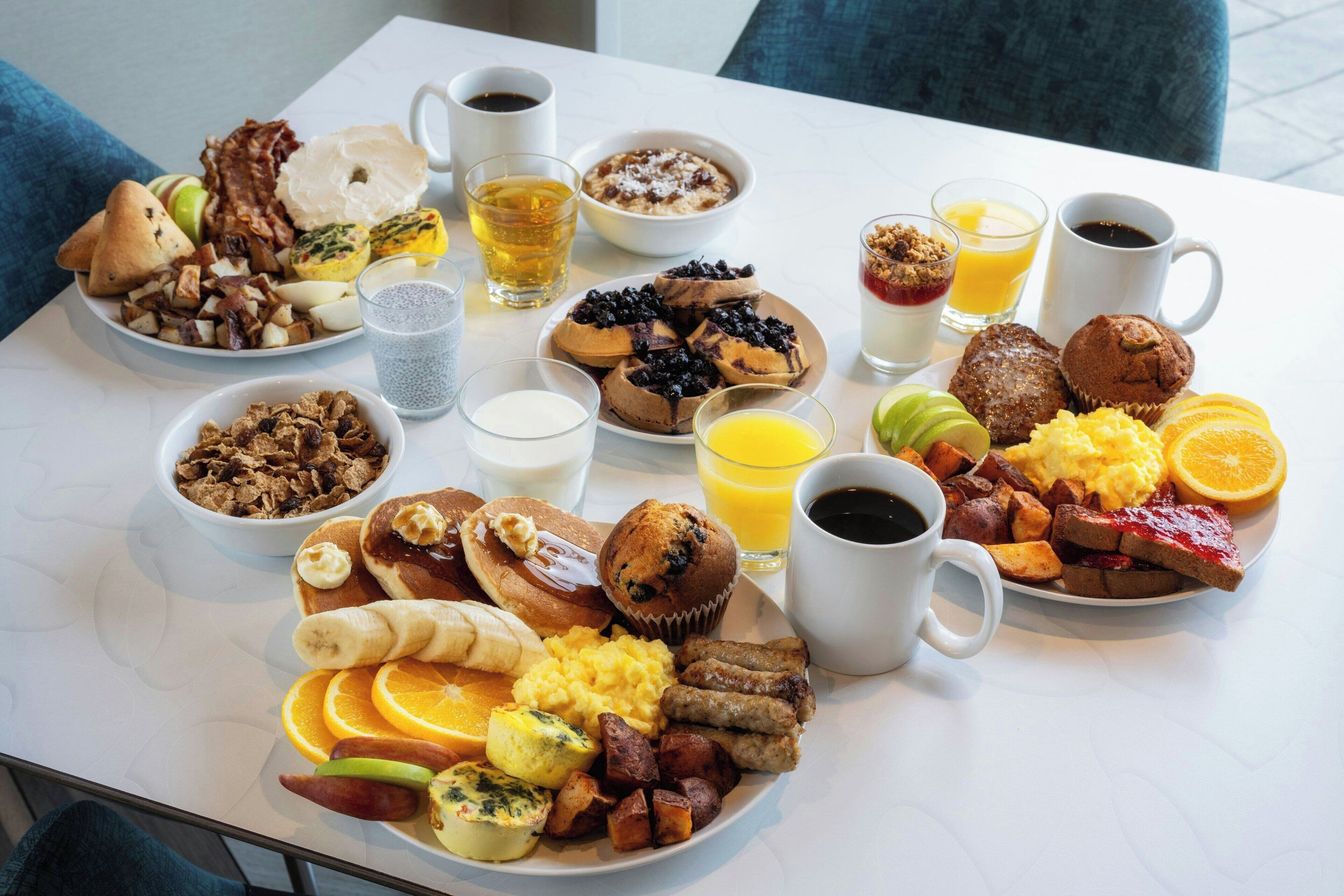 Una mesa blanca con una variedad de platos, bebidas y frutas para el desayuno.