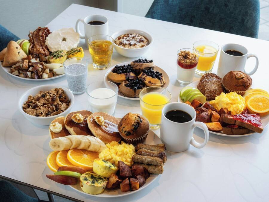 Una mesa blanca con una variedad de platos, bebidas y frutas para el desayuno.