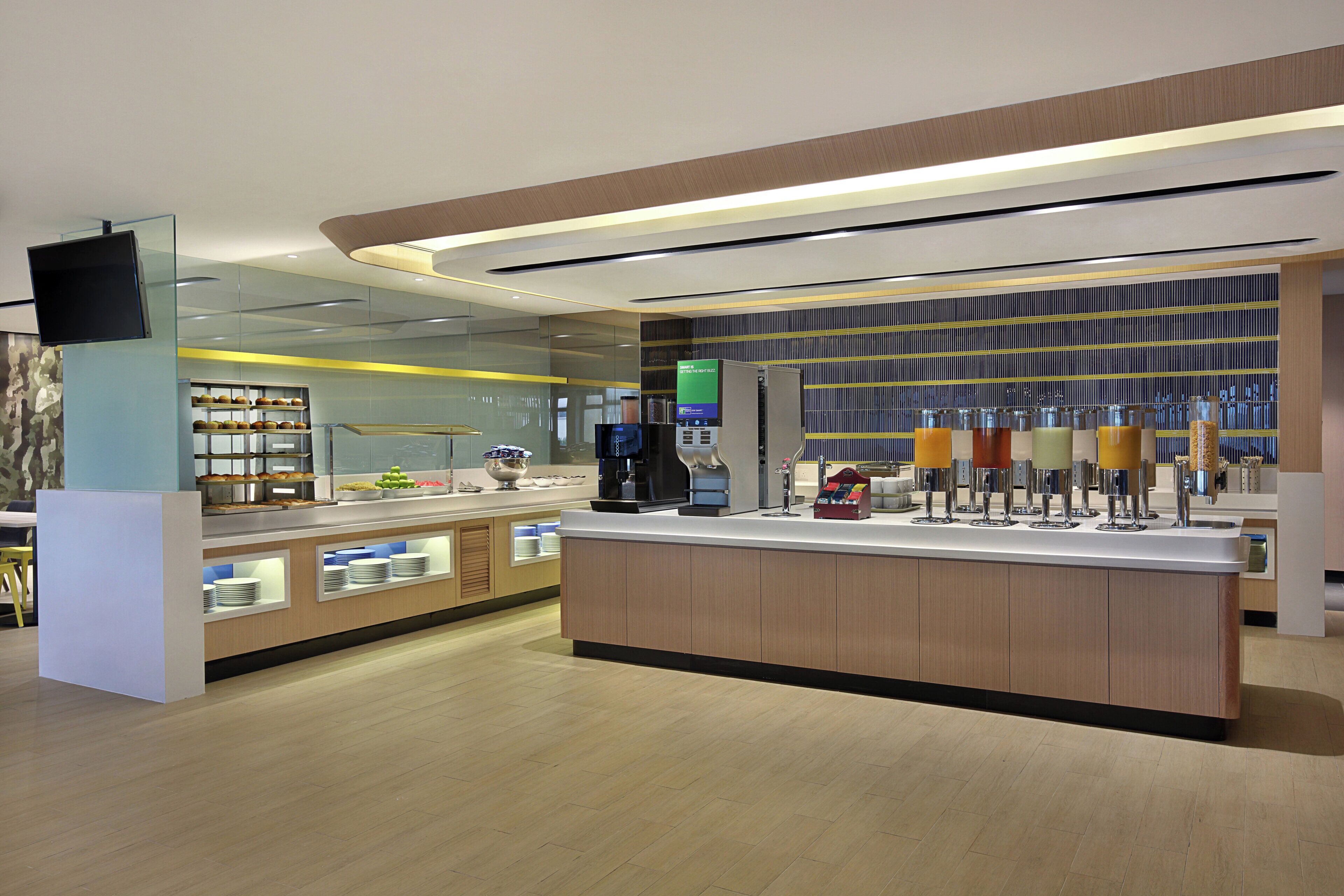 A modern cafe with a central counter, a coffee machine, and a variety of food items displayed.