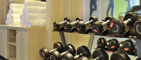 A rack of black dumbbells with weight markings, a towel stack, and a wall with silhouettes.
