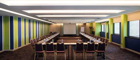 A conference room with a long table, chairs, and a projector screen.