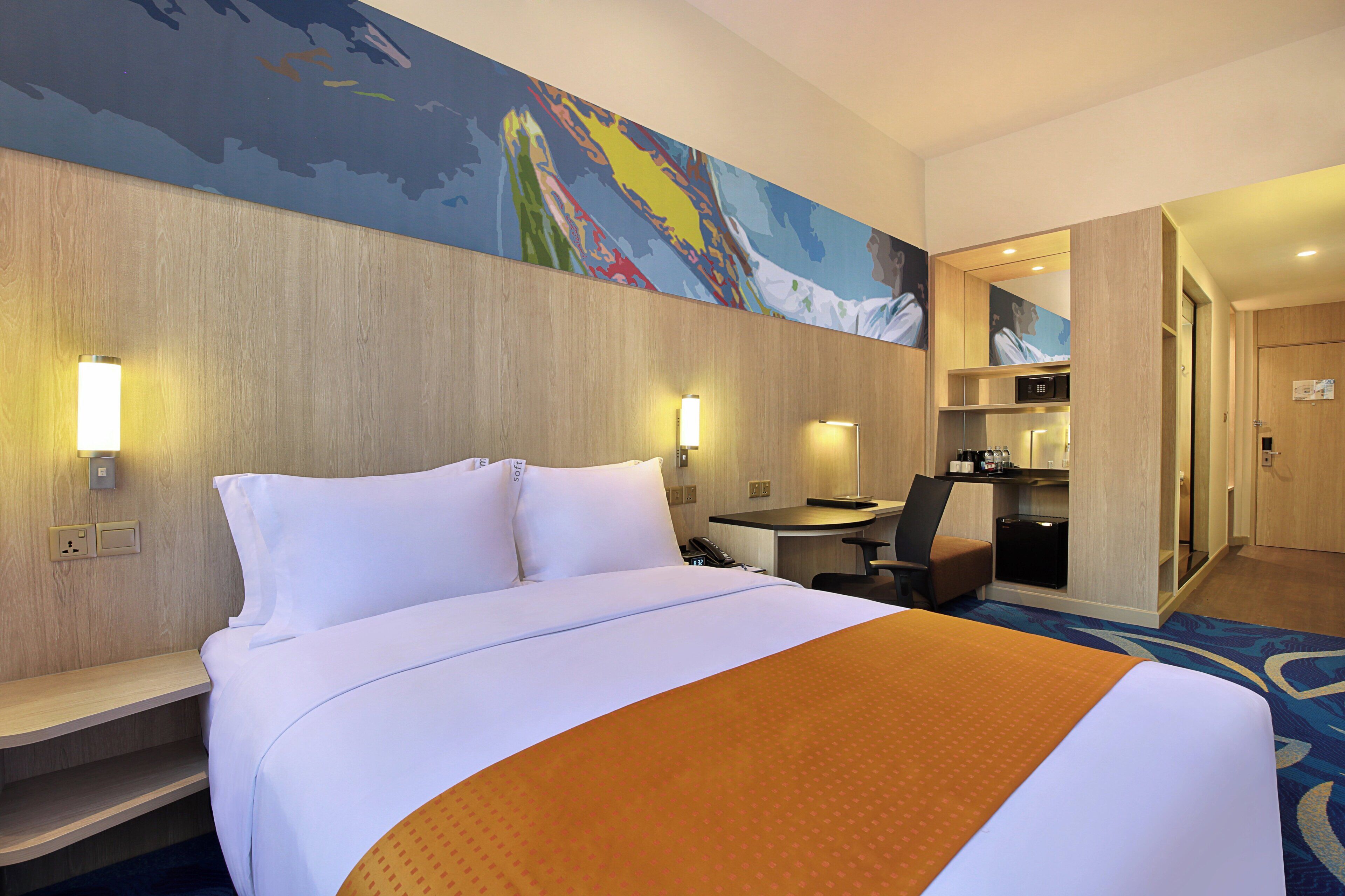 A hotel room with a large bed, a desk, and a chair. There is a microwave and a small kitchenette.