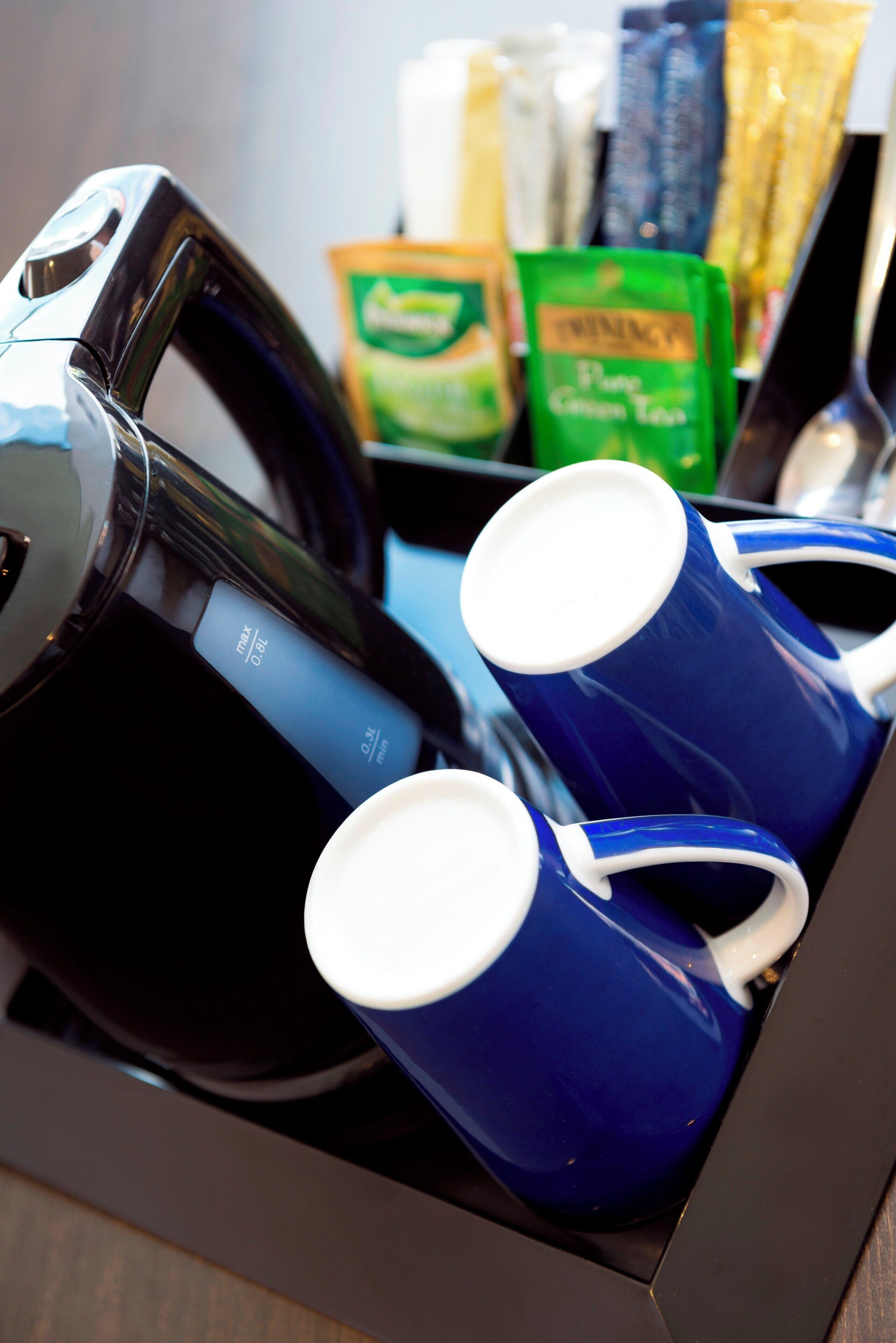 A coffee maker with two blue mugs and a green packet of tea.