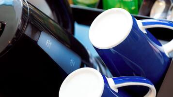 A coffee maker with two blue mugs and a green packet of tea.