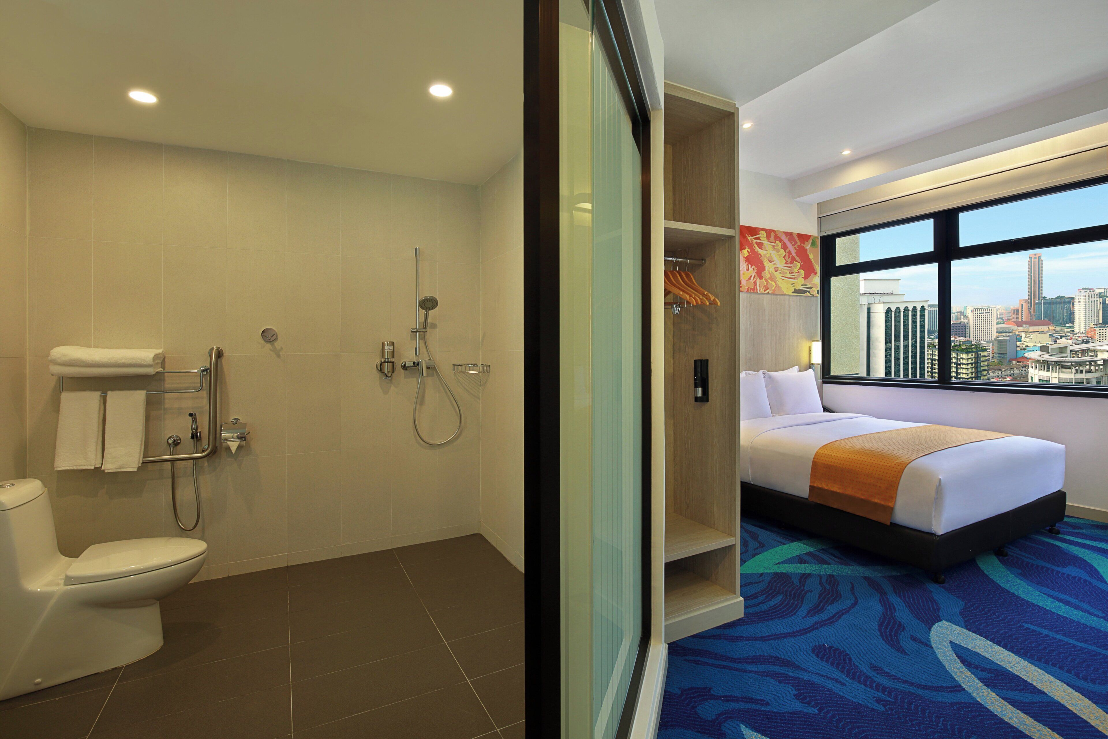 A hotel room with a shower, toilet, and a bed with a city view.