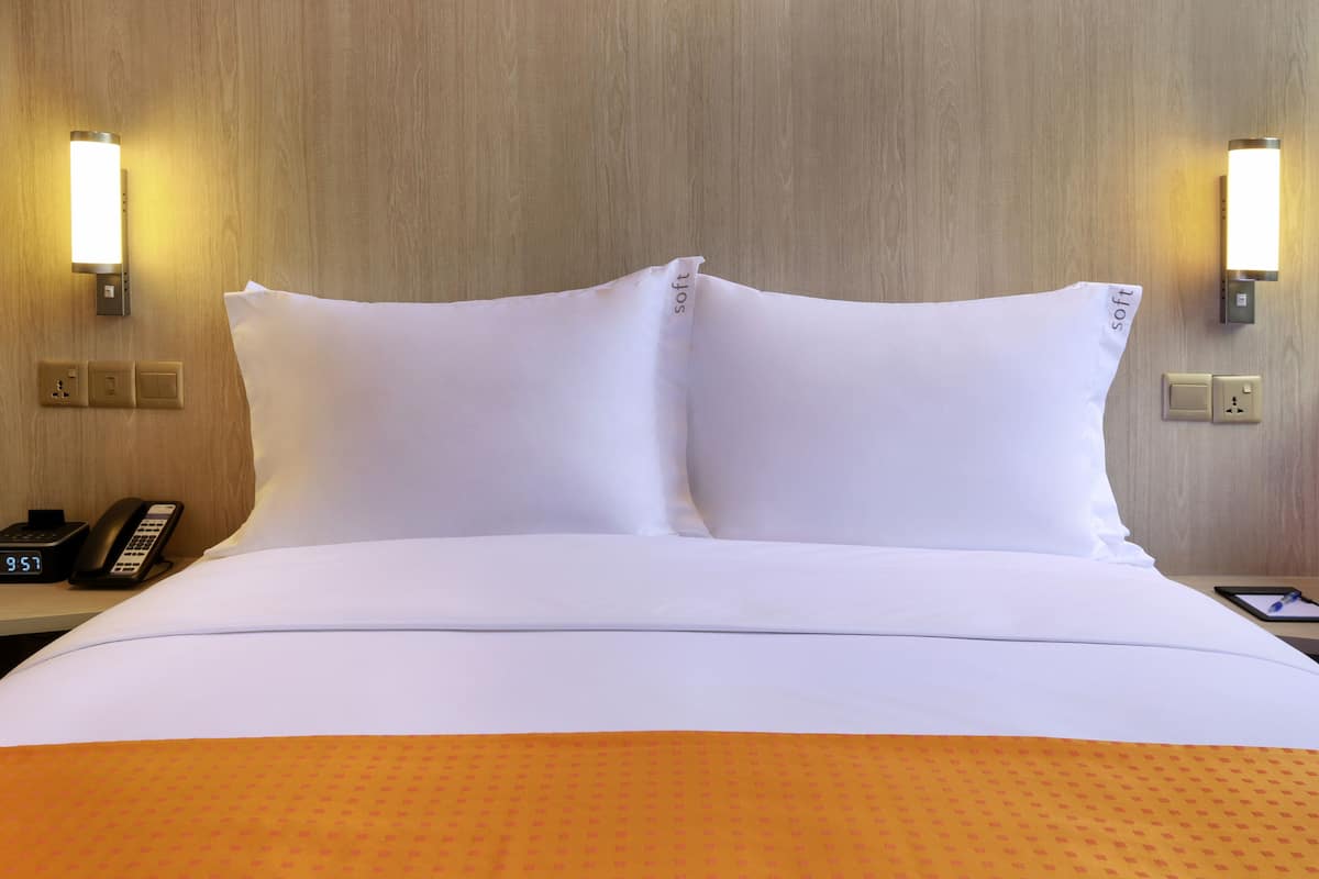 A hotel room with a neatly made bed, two bedside lamps, a bedside phone, and a tablet on the nightstand.