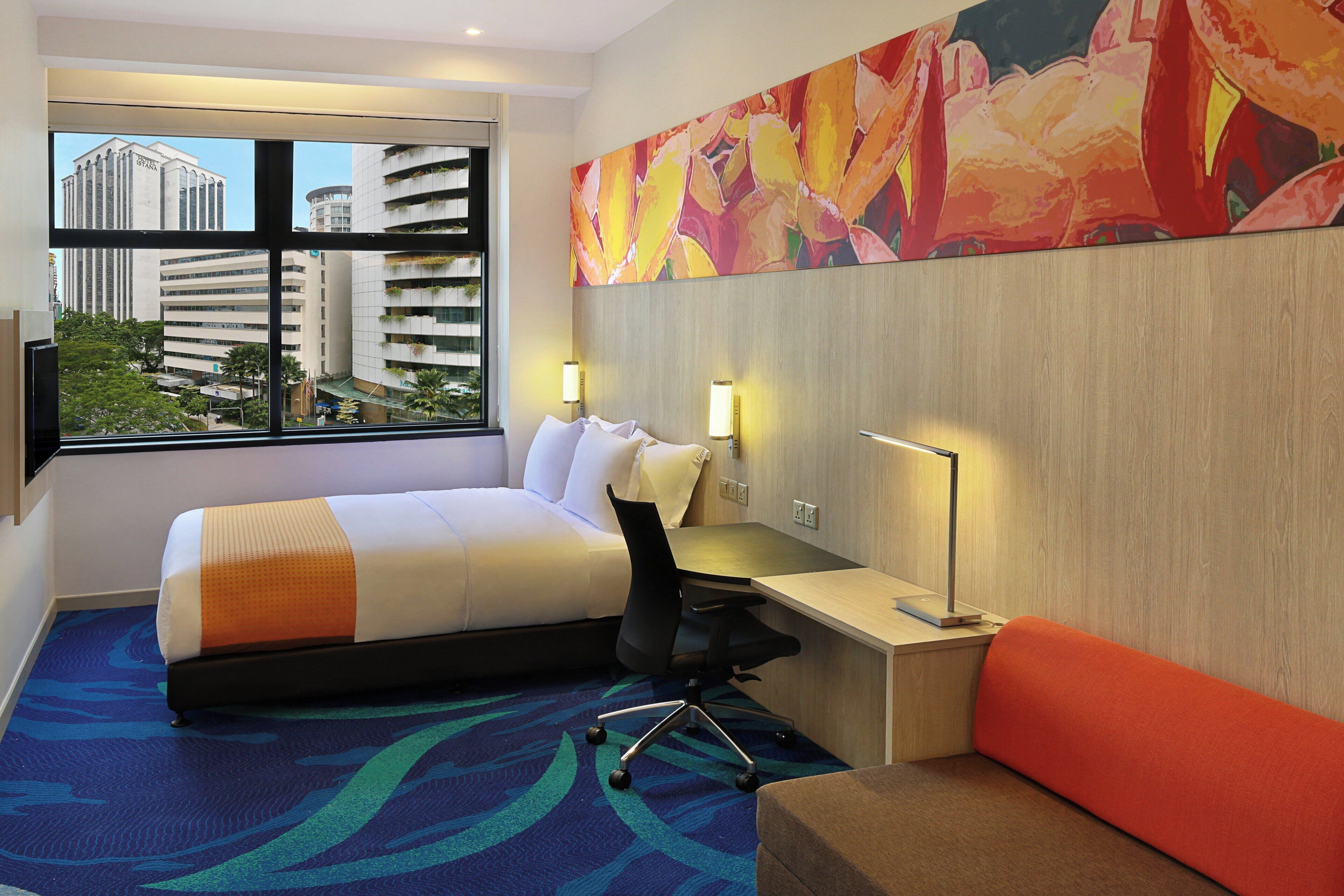 Une chambre d’hôtel équipée d’un lit, d’un bureau, d’une chaise et d’une grande fenêtre donnant sur la ville.