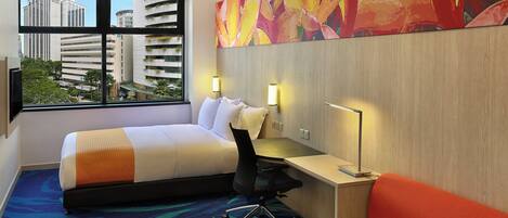 Une chambre d’hôtel équipée d’un lit, d’un bureau, d’une chaise et d’une grande fenêtre donnant sur la ville.