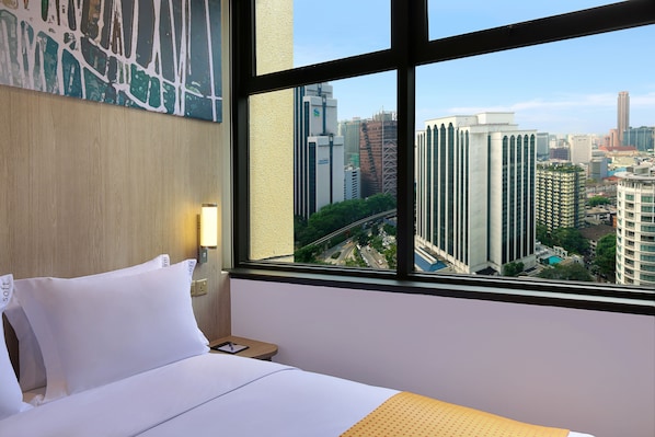 A hotel room with a bed, a nightstand, a lamp, and a large window offering a city view.