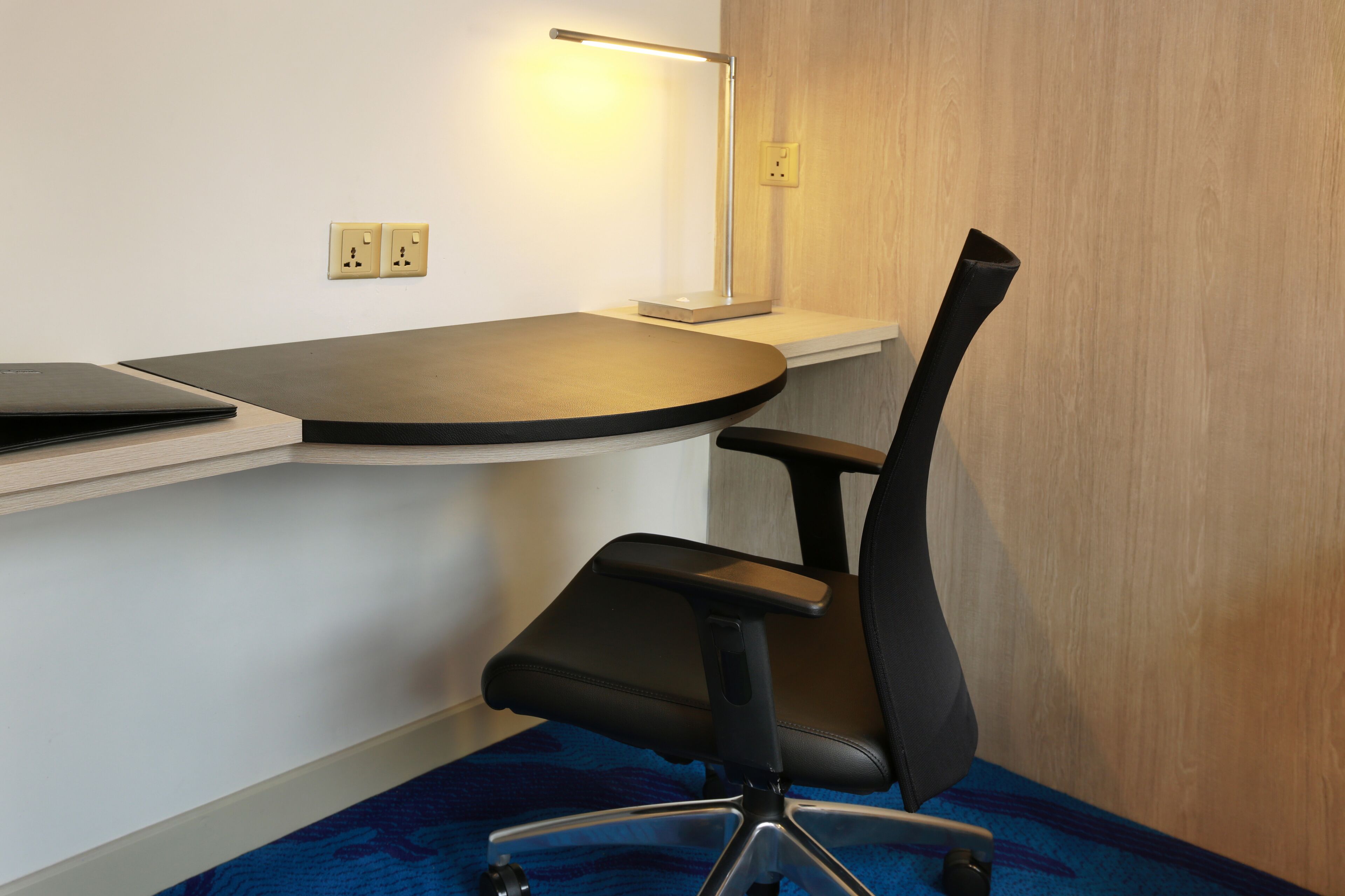 A corner office with a desk, chair, and lamp.