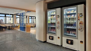 Um saguão de hotel moderno com área de estar, máquina de vendas automática e vista para a paisagem urbana.