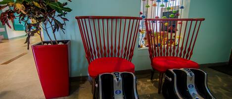 Una habitación con dos sillones rojos, una maceta roja con una planta y dos sillones de masaje.
