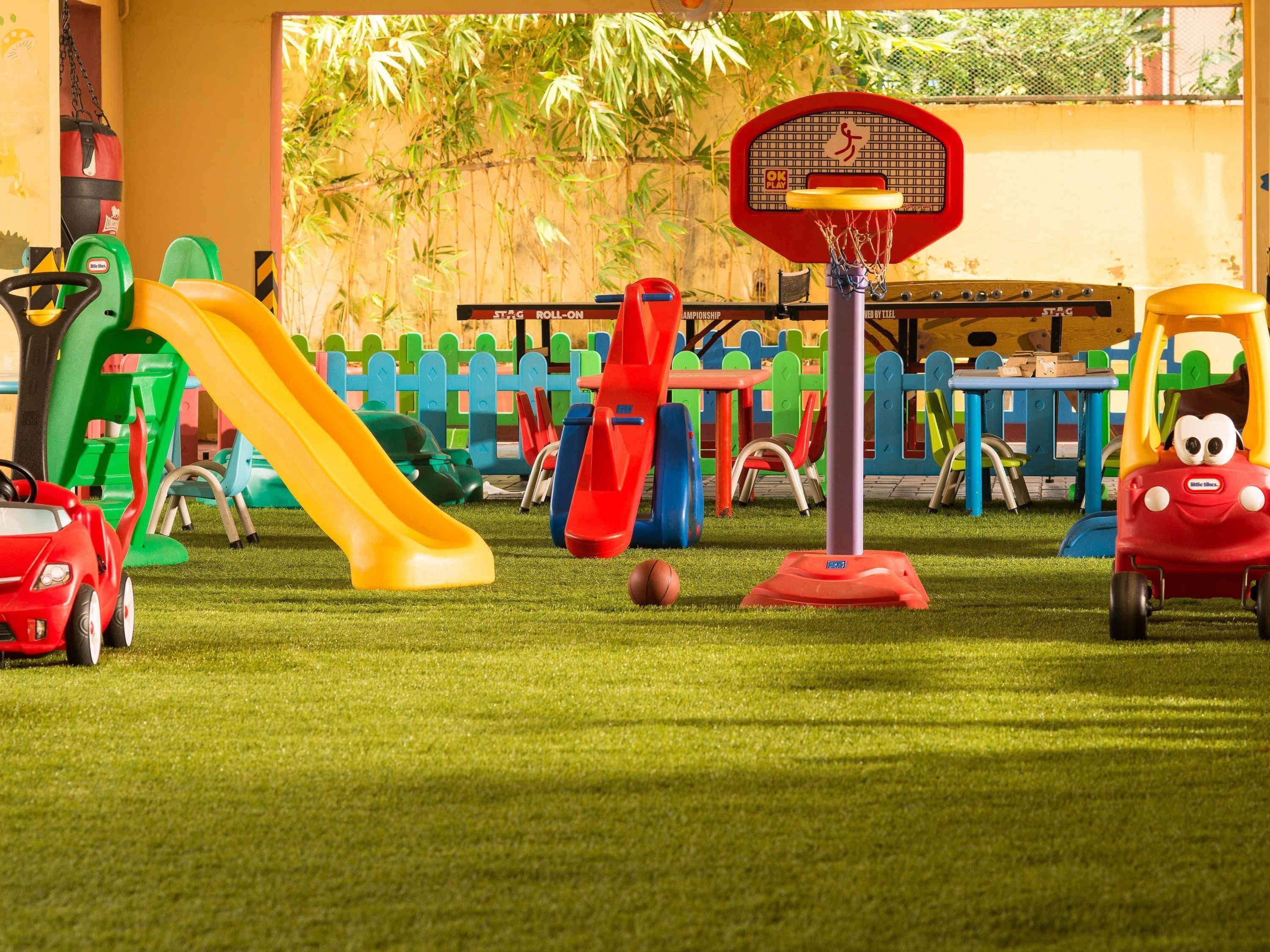Un espace de jeux pour enfants avec un panier de basket, des toboggans et des voitures jouets.