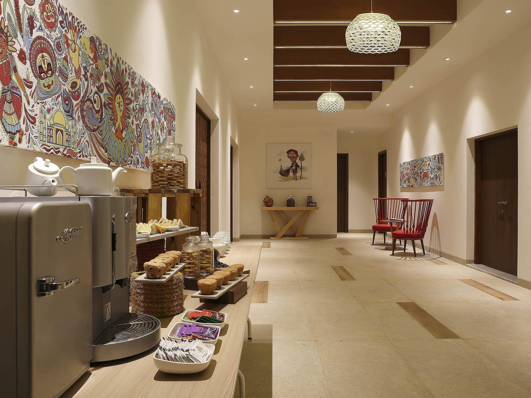A hotel corridor with a buffet, a coffee machine, and artwork on the walls.