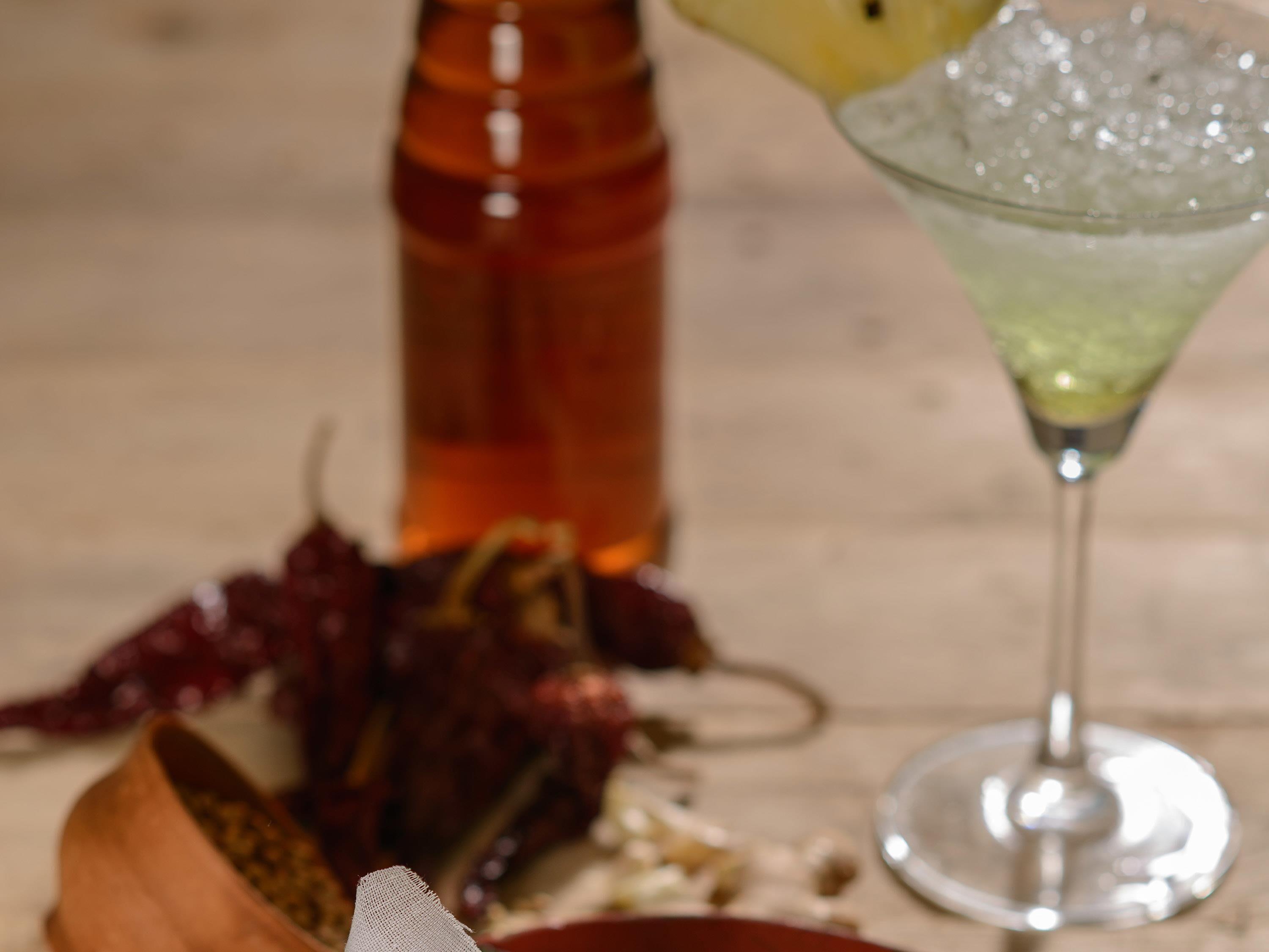 A bottle, a glass with a drink, and some food items on a table.
