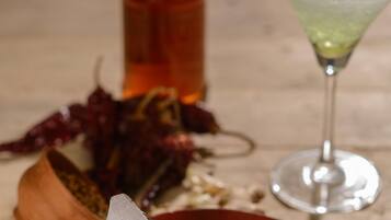 A bottle, a glass with a drink, and some food items on a table.