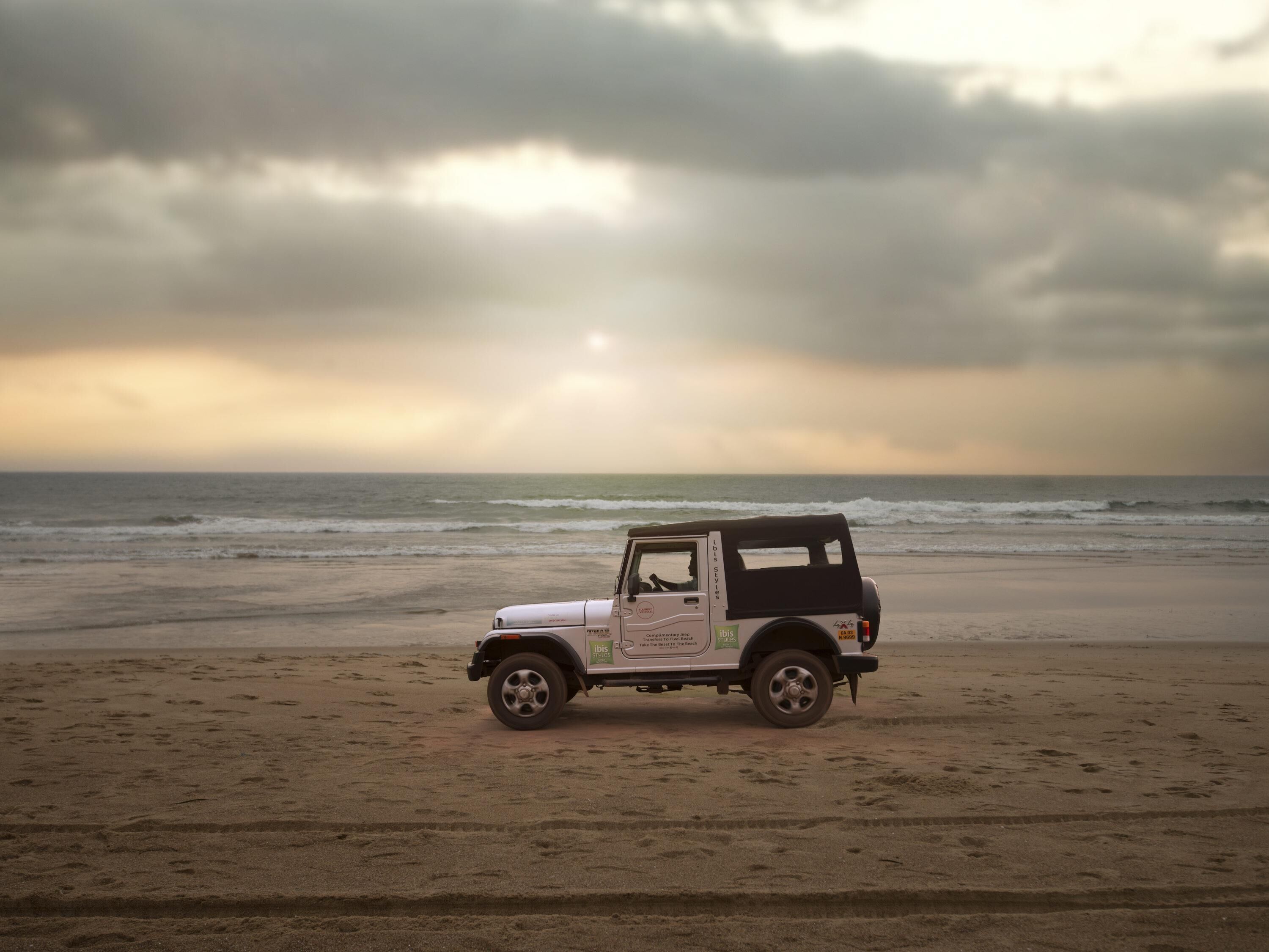 A white off-road vehicle parked on a sandy beach with the ocean in the background.