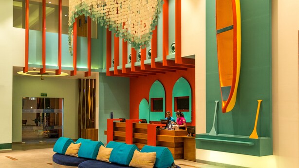 Un hall d’entrée spacieux avec un espace salon central, un escalier en colimaçon et un grand mur orné d’un motif coloré représentant une planche de surf.