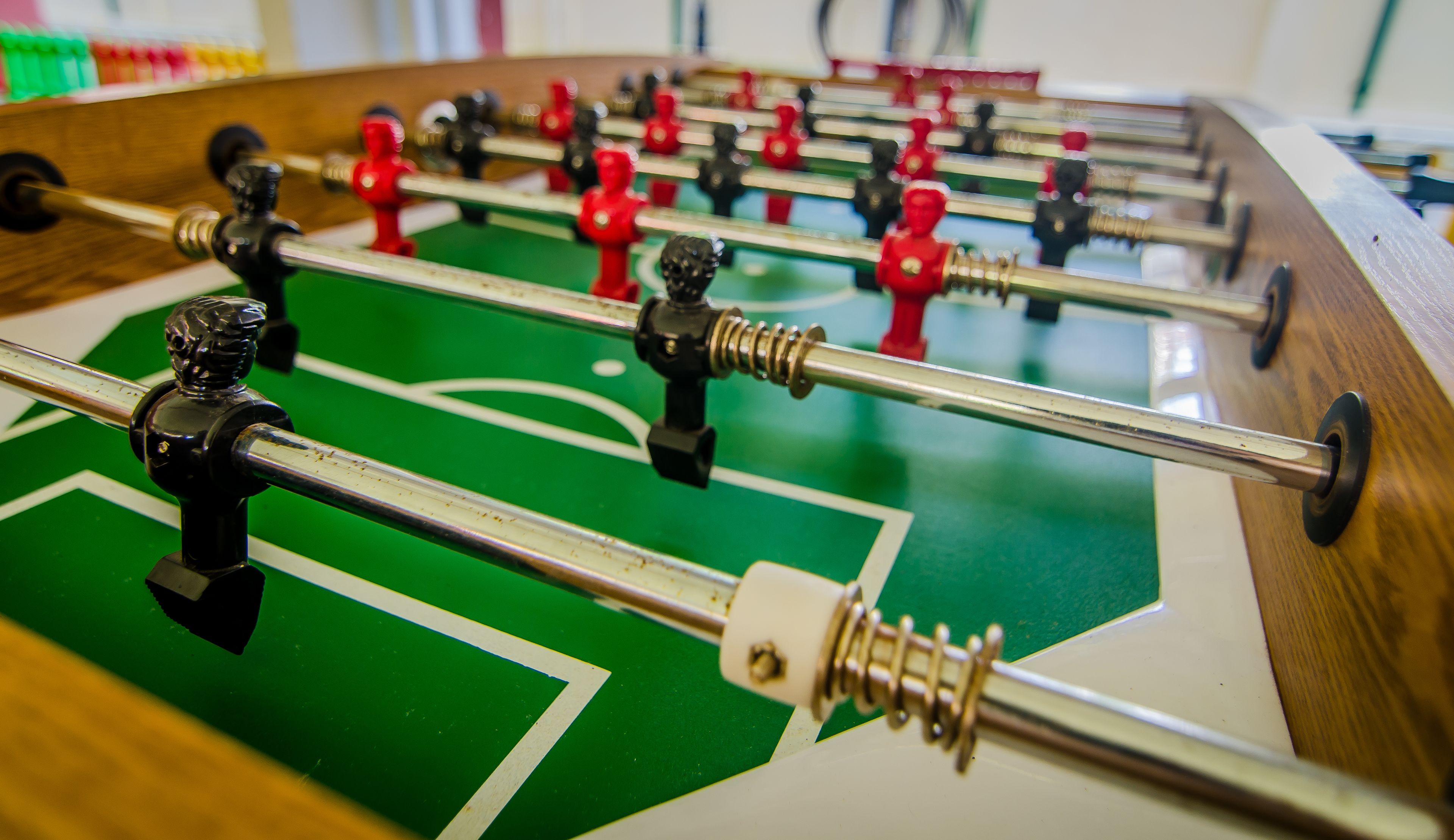 Primer plano de una mesa de fútbol de mesa con barras metálicas y figuras de jugadores rojas y negras.