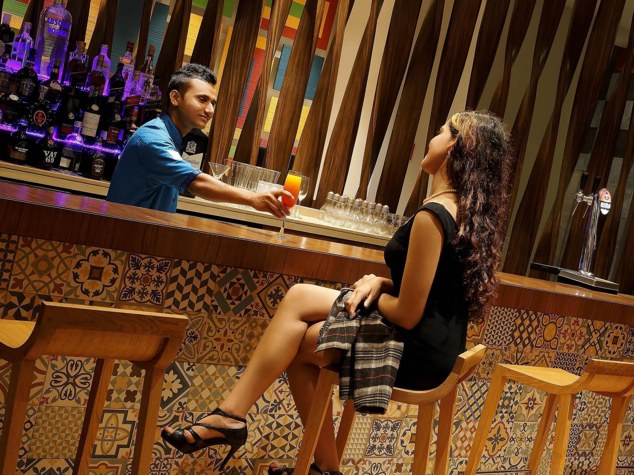 A bar area with a bartender and a seated woman, patterned tiles, and a bar counter with various bottles.