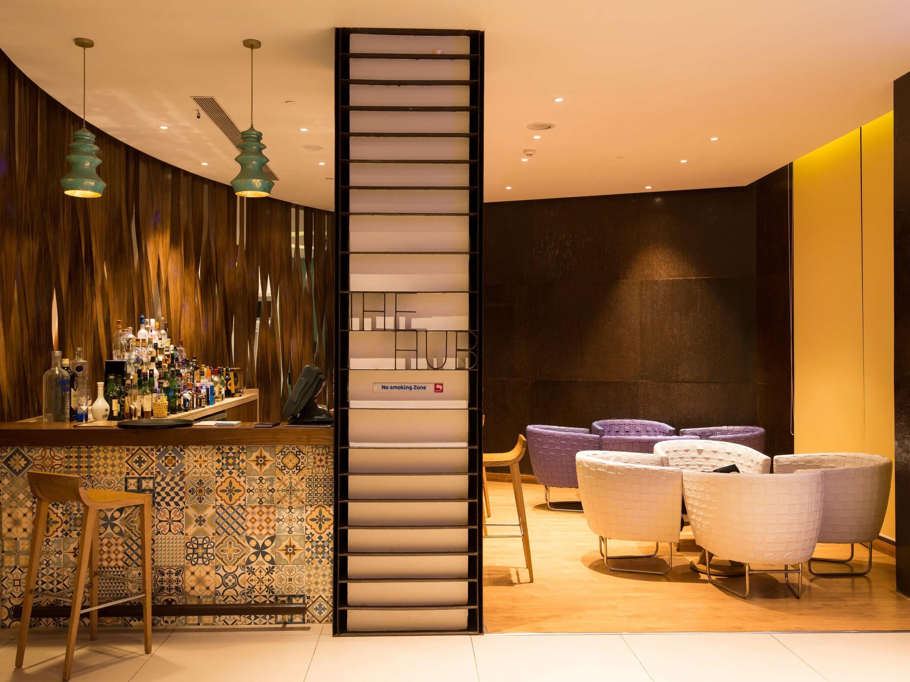 A modern bar area with a patterned tile backsplash, a wooden accent wall, and a seating area with cushioned chairs.