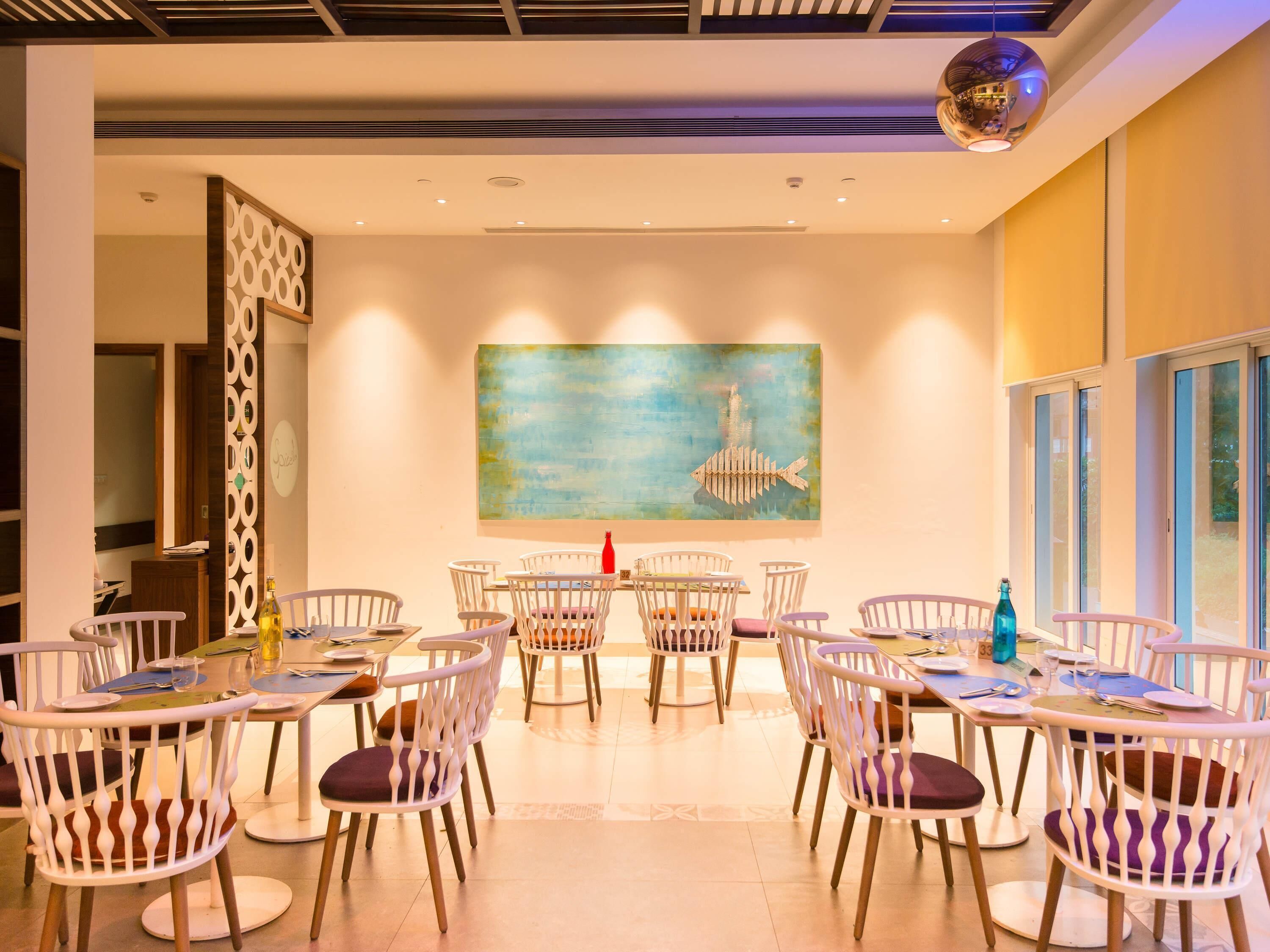 A dining area with white chairs, a table, and a painting of a fish on the wall.