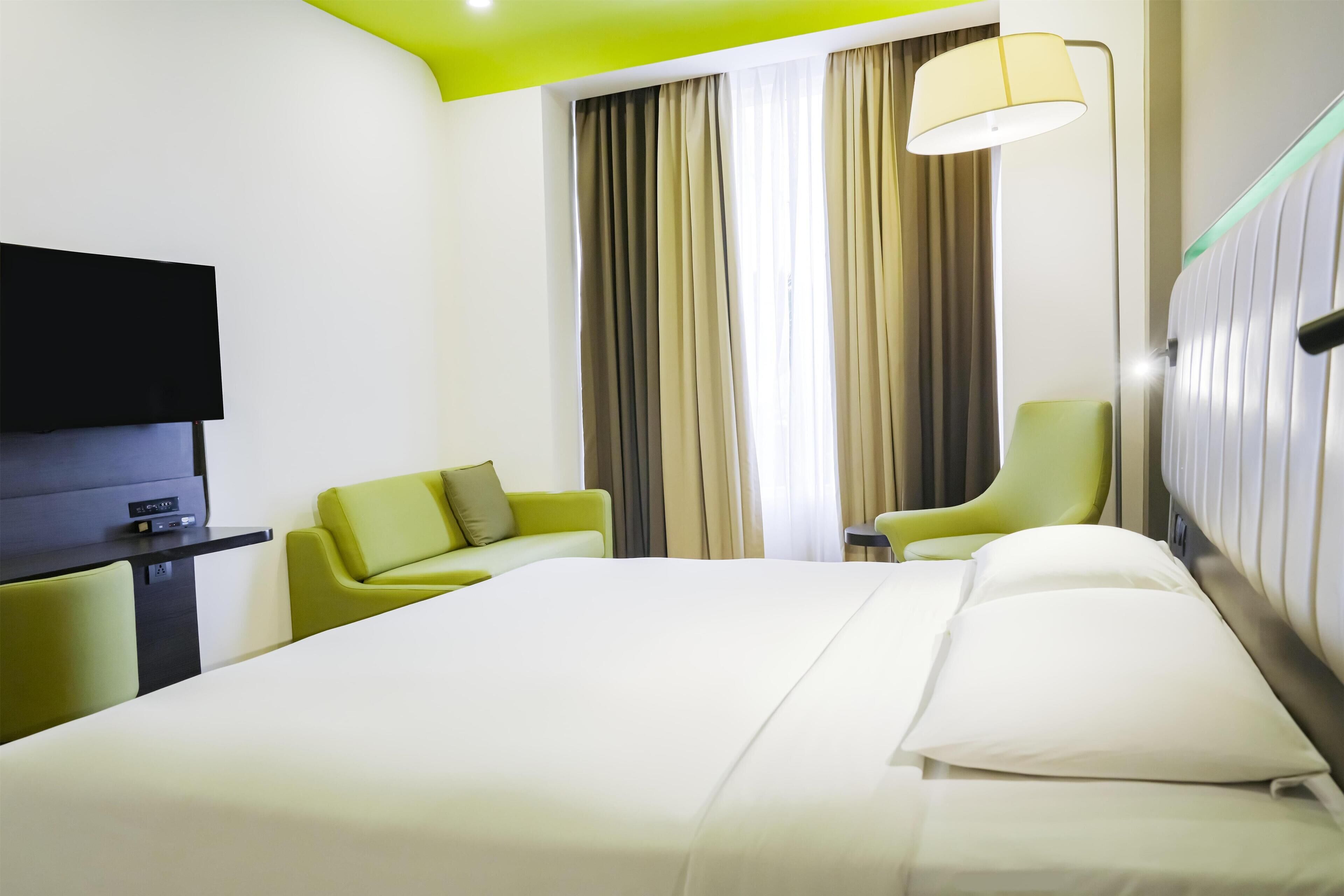 A hotel room with a bed, a TV, a desk, and two chairs.