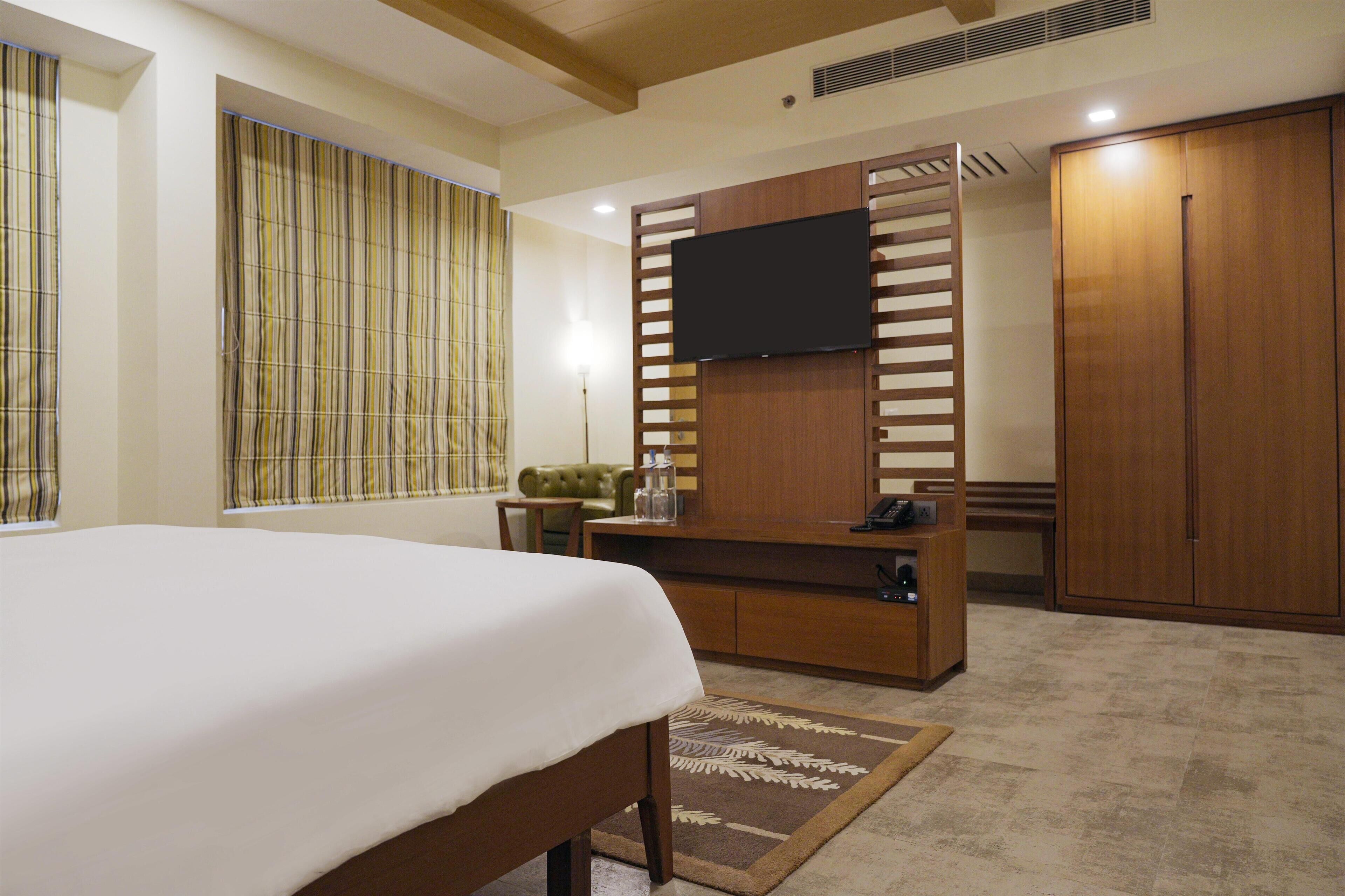 Ein Hotelzimmer mit Bett, Fernseher an einer Holzverkleidung, Kleiderschrank und einer kleinen Sitzecke mit Tisch und Stühlen.