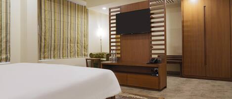 A hotel room with a bed, a TV mounted on a wooden panel, a wardrobe, and a small seating area with a table and chairs.