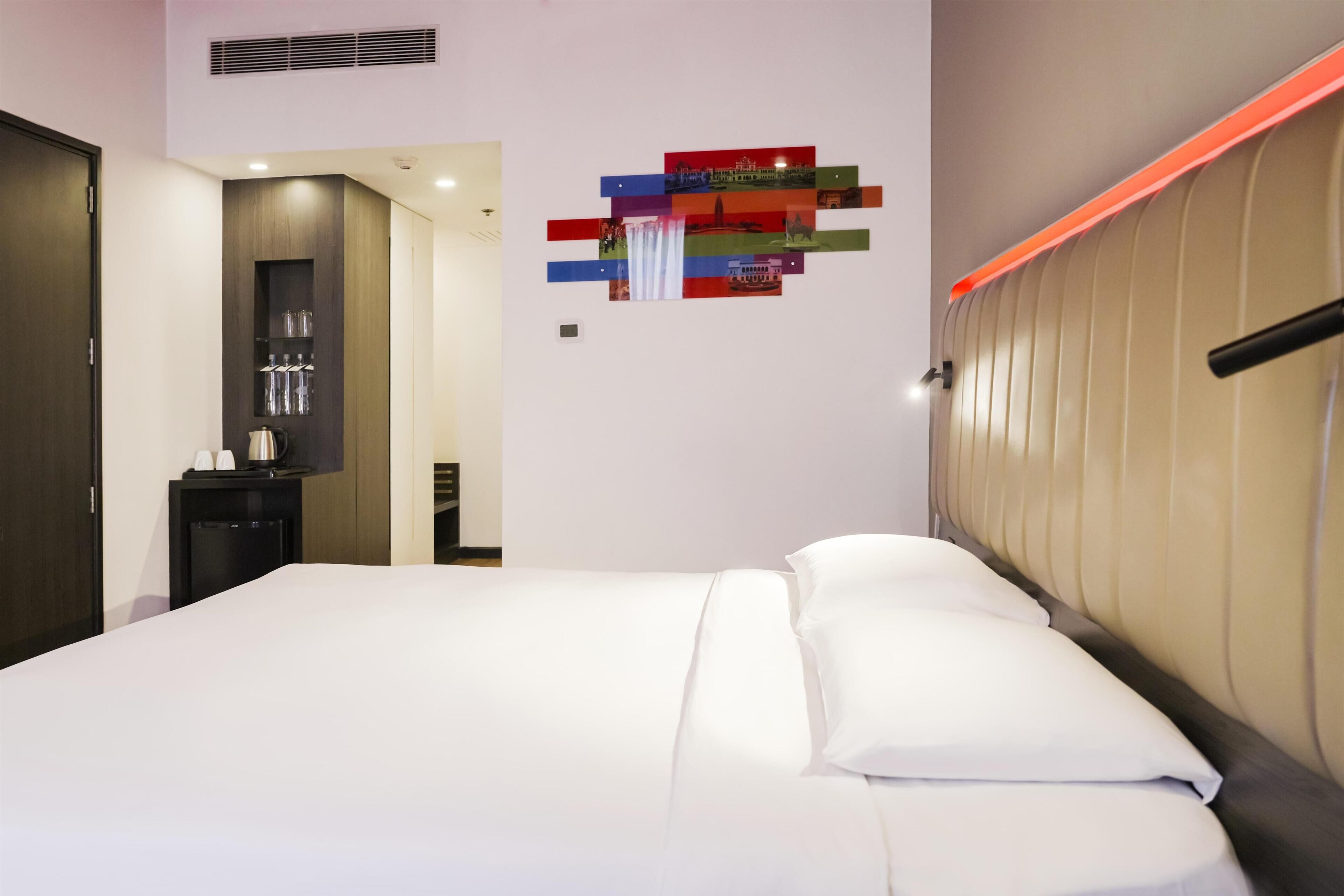 A modern hotel room with a large bed, a bedside table, and a wall-mounted artwork.