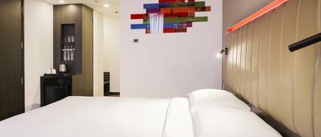 A modern hotel room with a large bed, a bedside table, and a wall-mounted artwork.