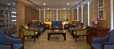 A hotel lobby with a central seating area, a patterned carpet, and a decorative wall.