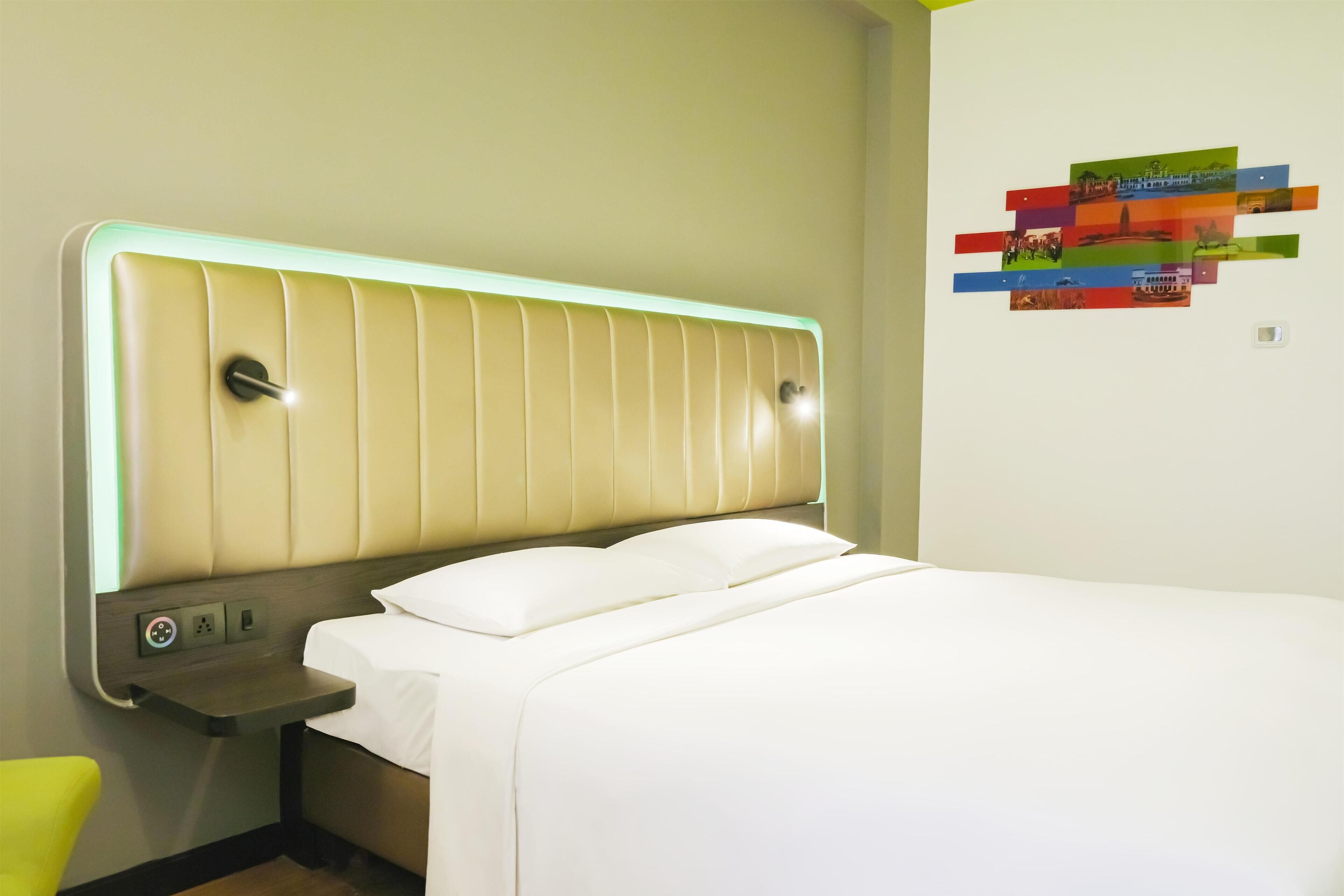 Una habitación de hotel con una cama, una mesita de noche y una lámpara fijada a la pared.