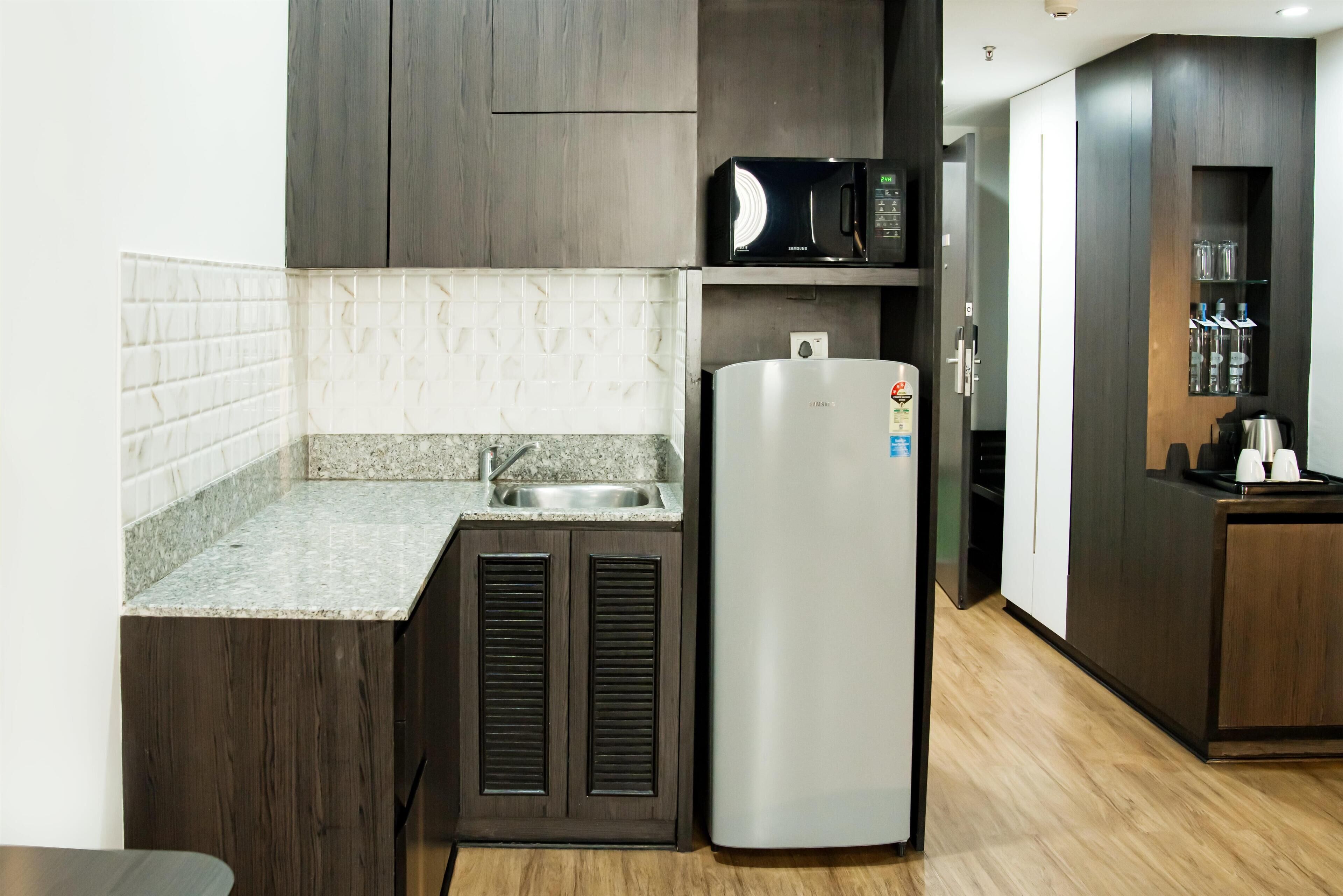 A modern kitchen with dark wood cabinets, a stainless steel refrigerator, a microwave, and a built-in sink.