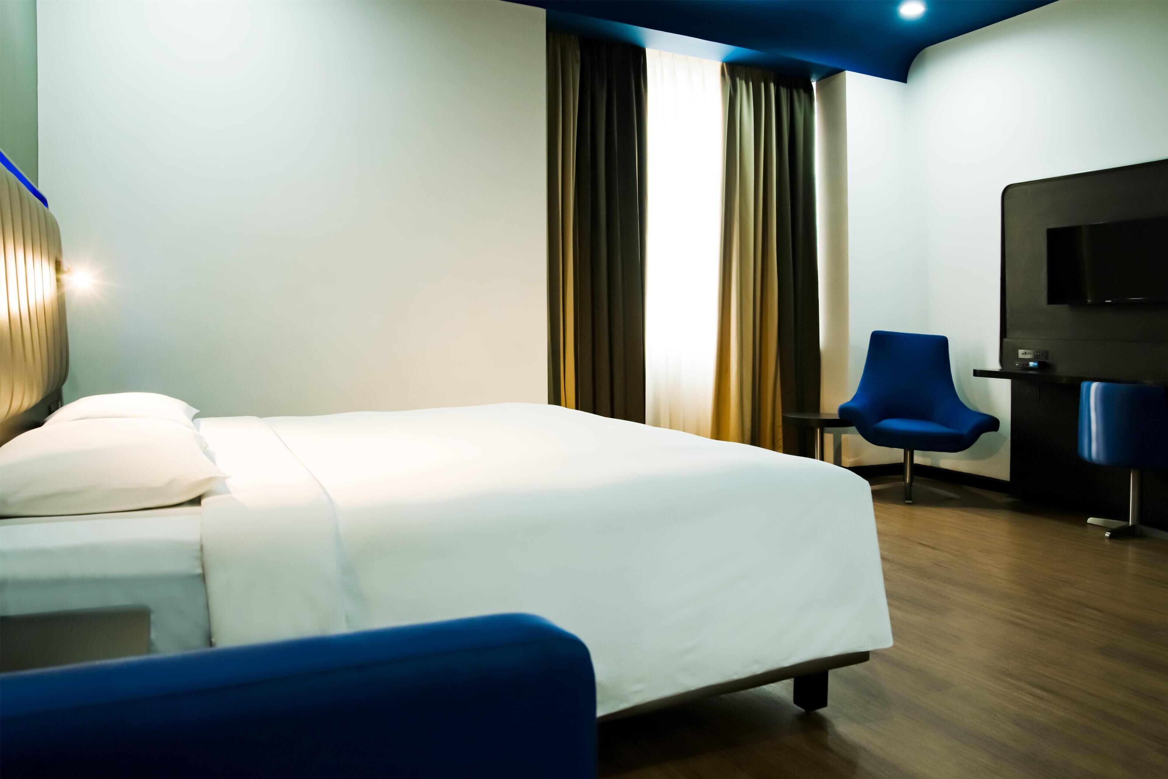 A hotel room with a bed, a blue chair, a TV, and a desk.