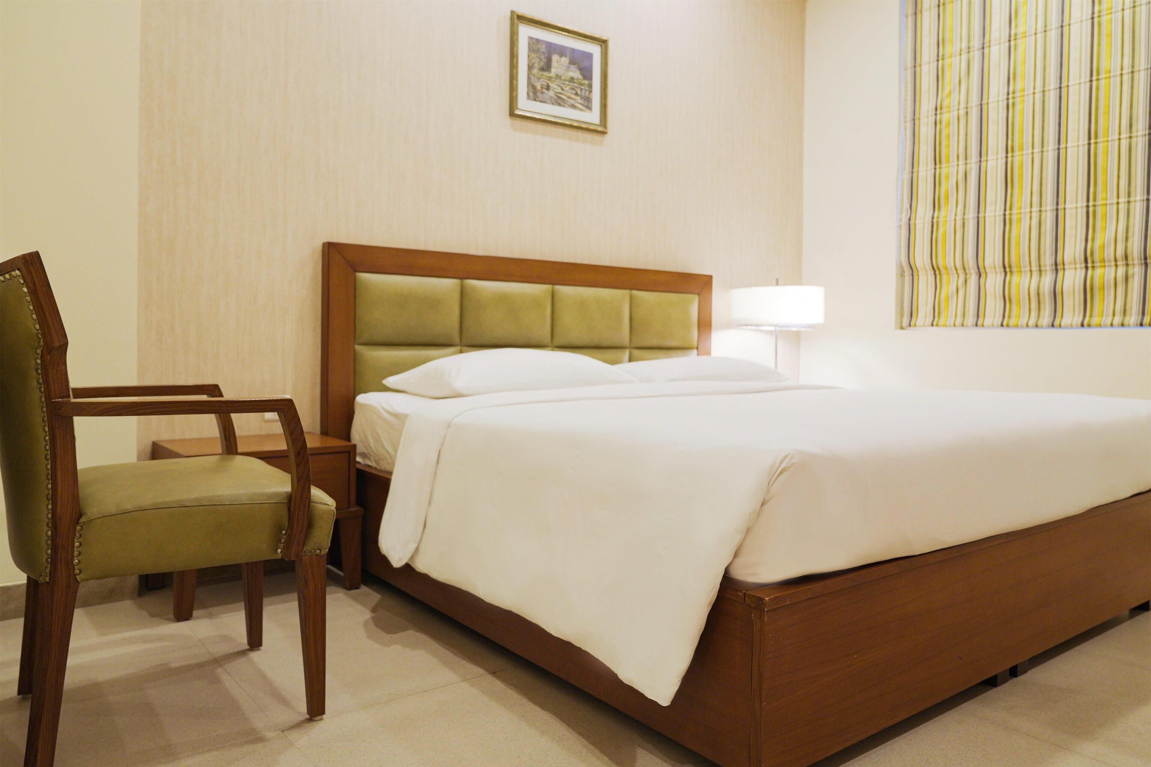 A hotel room with a bed, a chair, a nightstand, and a lamp.