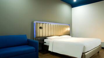 Una habitación de hotel moderna con cama, mesita de noche y un sillón azul.