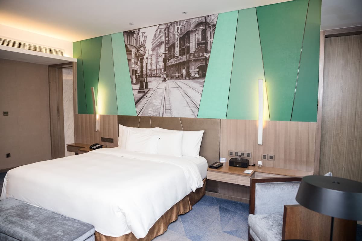 A modern hotel room with a large bed, a desk with a lamp, and a wall-mounted picture of a street scene.
