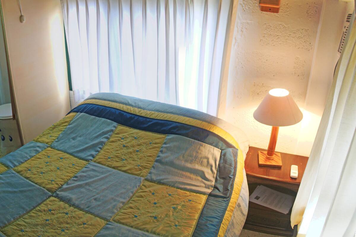 Hotelkamer met een bed, een bedlampje, een raam met gordijnen, een badkamer met een wastafel en toilet, en een wandradiator.